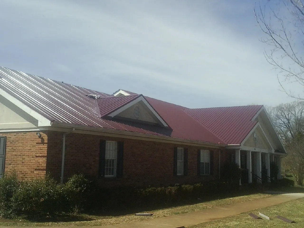Red metal roof with gabled entries on a long brick building, from a Hail Damage Roof Repair job in Rocklin