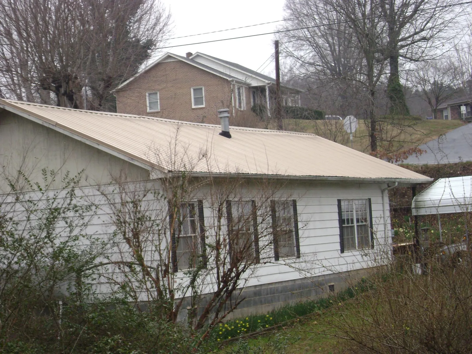 Tan metal roof on a white sided house set into a hillside — Commercial Roofing by Roofing Brothers in Rocklin